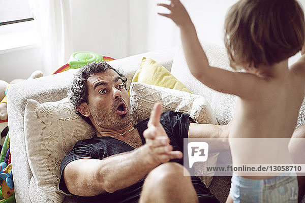Father playing with daughter while lying on sofa at home
