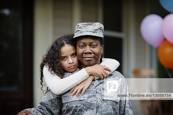 Portrait of daughter embracing soldier against house