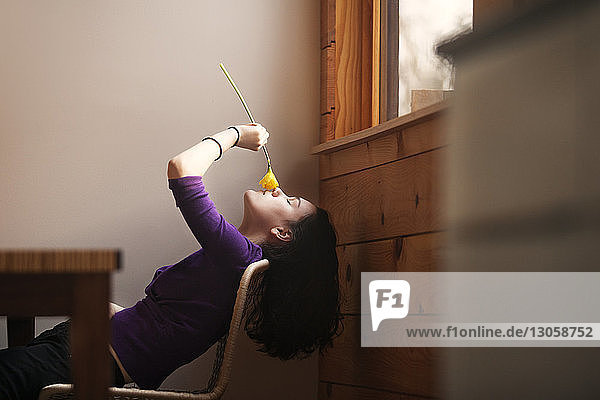 Seitenansicht einer Teenagerin  die zu Hause auf einem Stuhl sitzend an einer Blume riecht