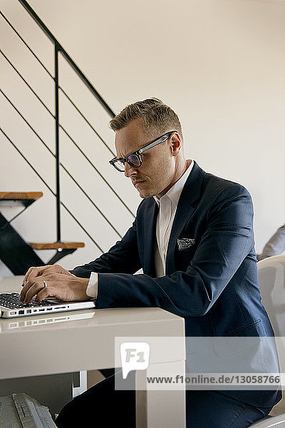Geschäftsmann benutzt Laptop  während er im Büro am Tisch sitzt