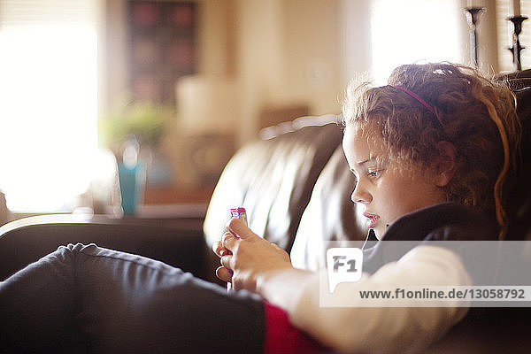 Mädchen benutzt Mobiltelefon  während sie zu Hause auf dem Sofa liegt