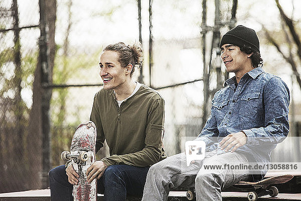 Smiling friends looking away while sitting at skateboard park