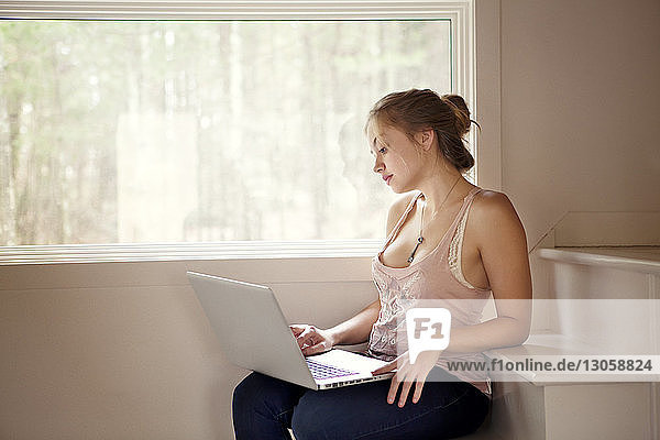 Woman using laptop computer while sitting on steps at home