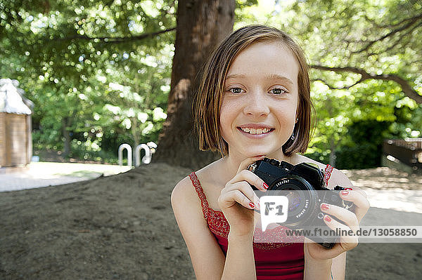 Portrait of girl holding camera while standing at backyard