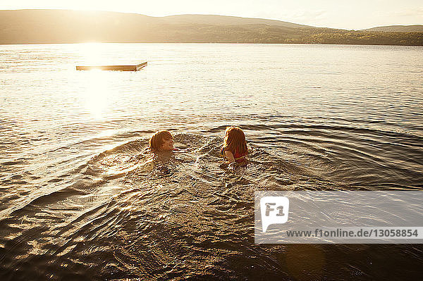 Glückliche Geschwister schwimmen bei Sonnenuntergang im See