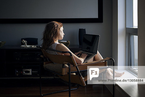 Woman using laptop while sitting on chair at home
