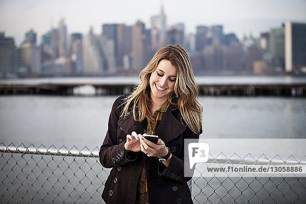 Glückliche junge Frau benutzt Telefon gegen Fluss in der Stadt