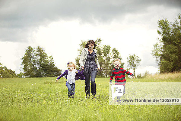 Happy mother walking with children on grassy field against sky