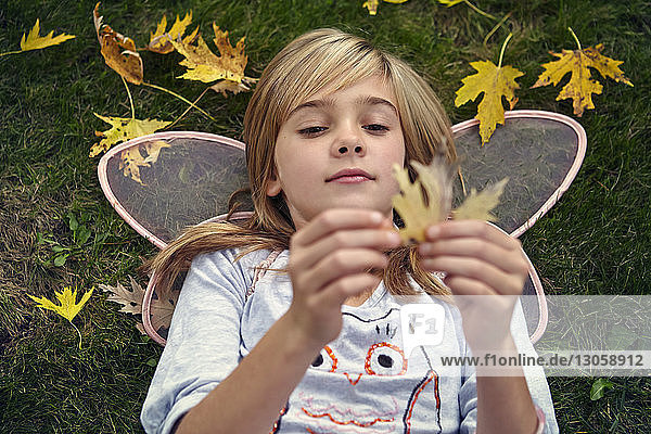 High angle view of girl in fairy costume holding leave while ly8ing on filed