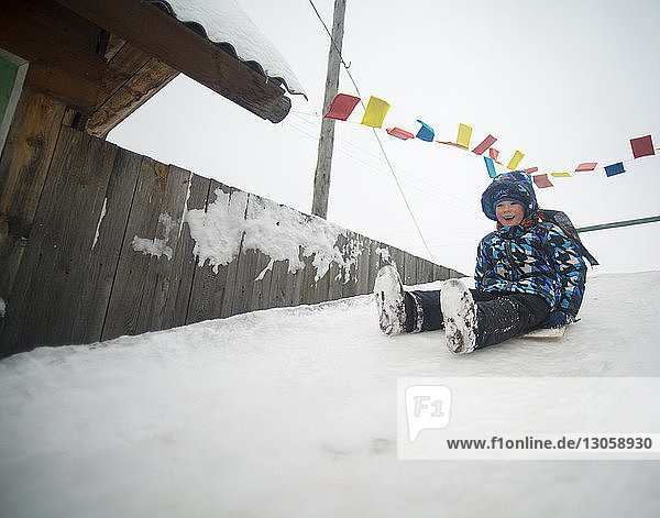 Glücklicher Junge rodelt auf schneebedecktem Hügel