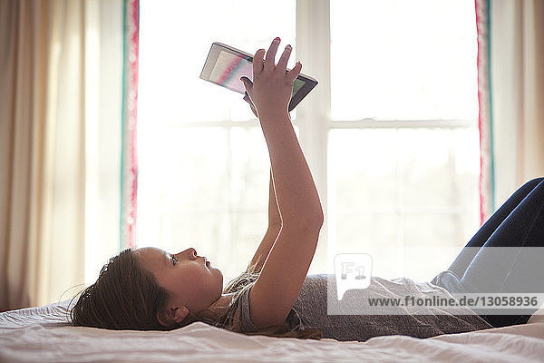 Seitenansicht eines Mädchens  das die Tablette benutzt  während es zu Hause auf dem Bett liegt