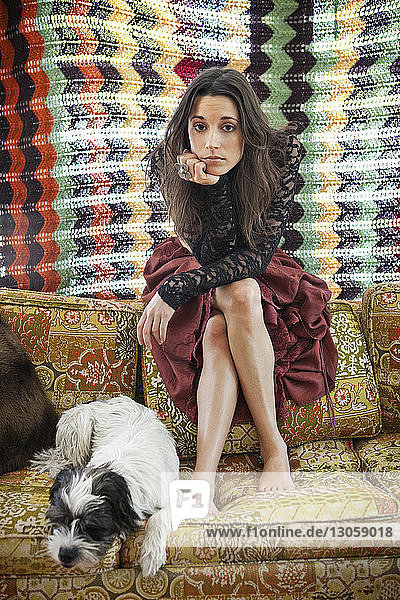 Porträt einer Frau  die zu Hause auf einem Sofa mit Hund sitzt