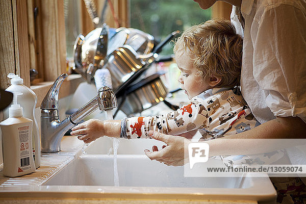 Ausgeschnittenes Bild einer Mutter  die ihrem Sohn beim Händewaschen an der Küchenspüle hilft