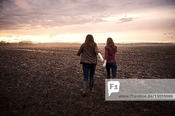 Rear view of female friends walking on field against sky during sunrise