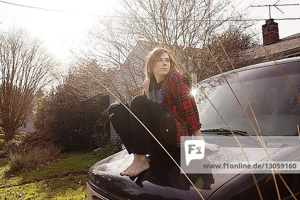 Nachdenkliche Frau sitzt auf Auto gegen klaren Himmel