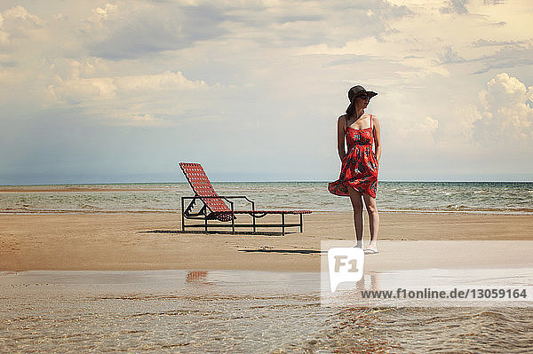 Frau schaut weg  während sie am Strand am Liegestuhl steht