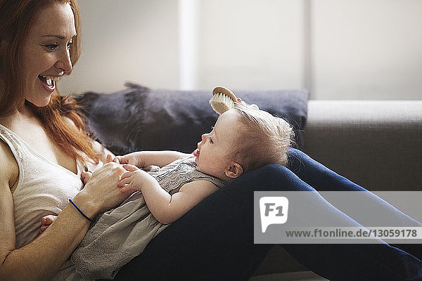 Cropped image of mother brushing baby girl's hair while sitting on sofa at home