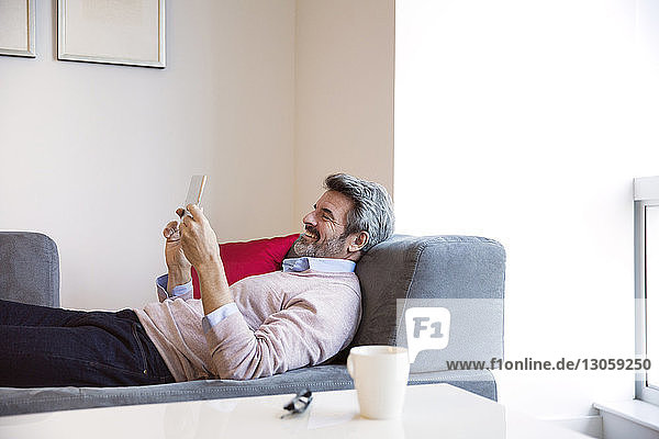 Smiling businessman looking at tablet computer while lying on sofa