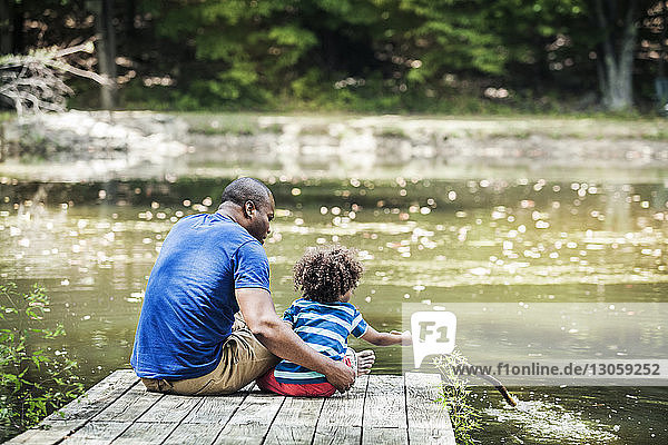 Father looking at son playing with stick at lake