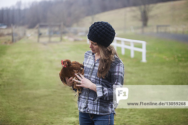 Frau trägt Henne  während sie auf dem Bauernhof steht