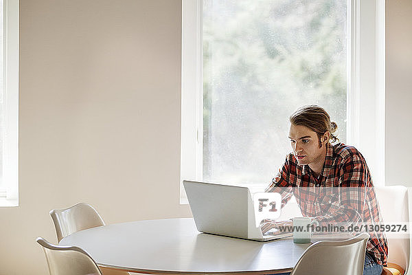 Man using laptop at table by window
