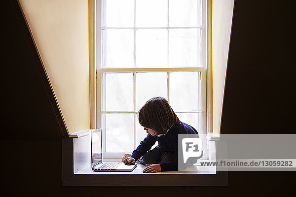 Junge benutzt Laptop-Computer  während er sich zu Hause auf den Boden lehnt