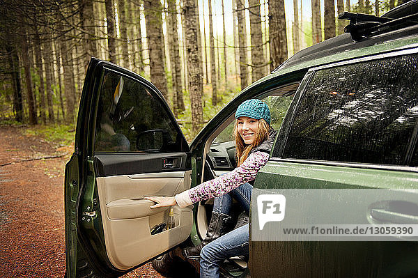 Porträt einer glücklichen Frau  die im Wald aus dem Auto steigt