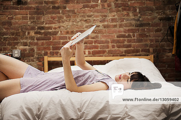 Junge Frau liegt auf dem Bett und benutzt zu Hause ein digitales Tablett