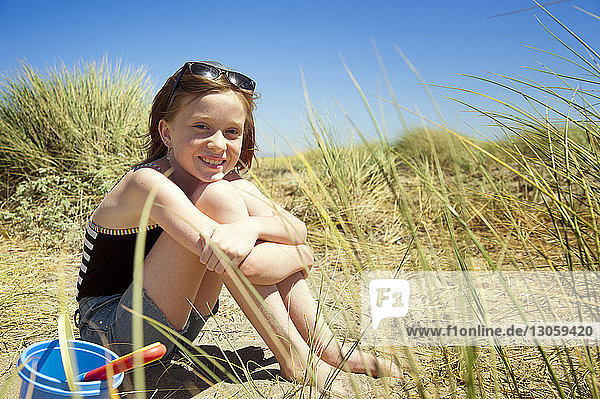 Porträt eines glücklichen Mädchens  das auf Sand vor klarem Himmel sitzt