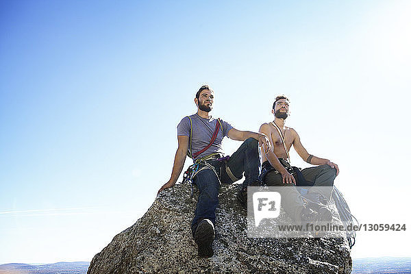 Freunde sitzen auf einem Felsen vor klarem Himmel