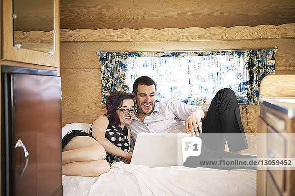 Lächelndes Paar benutzt Laptop-Computer  während es im Wohnmobil im Bett sitzt