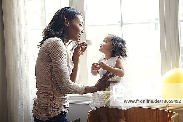 Woman playing with daughter by window at home
