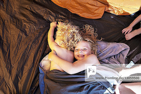 Hochwinkelansicht der Geschwister  die im Schlafsack am Zelt ruhen