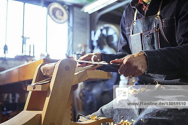Mittelteil eines Zimmermanns beim Rasieren von Holz mit Ziehmesser in der Werkstatt