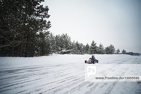 Man enjoying go-carts racing on snow covered field against sky