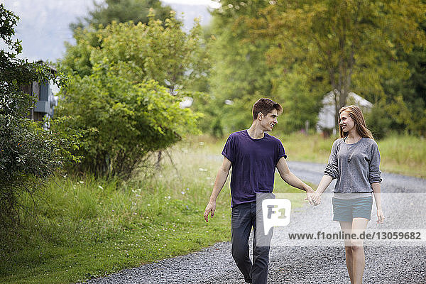 Glückliches Paar hält sich an den Händen  während es auf einer Schotterstraße durch ein Feld läuft