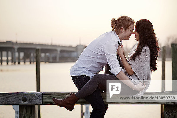 Happy romantic couple sitting on railing against sky