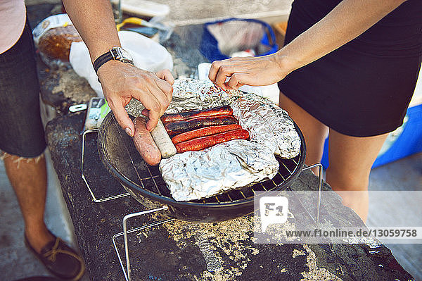 Schrägansicht von Freunden die Würstchen auf dem Grill zubereiten