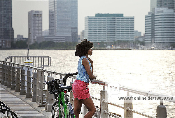 Side view of woman looking away while standing by railing at promenade