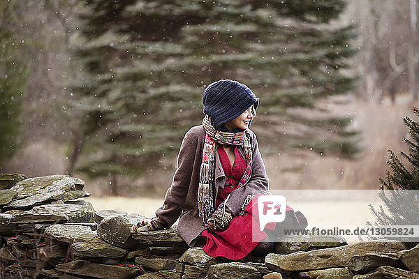 Happy woman looking away while relaxing on stone wall