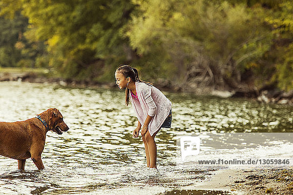 Side view of smiling girl looking at dog in lake