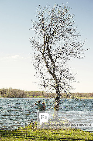 Rear view of couple standing by bare tree at riverbank