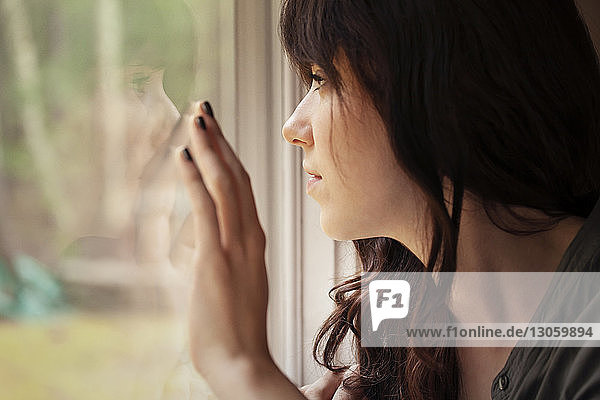 Nahaufnahme einer Frau  die zu Hause durch ein Fenster schaut