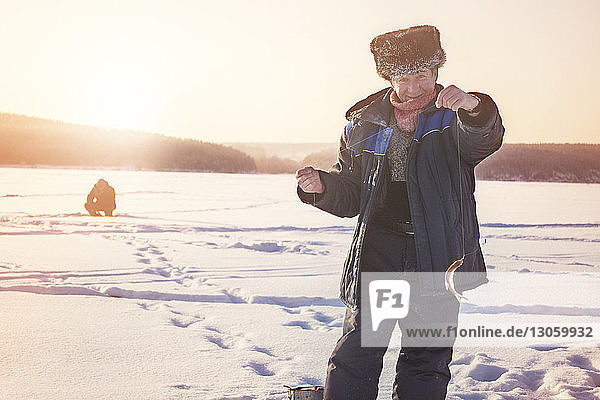 Portrait of senior man holding fish while standing on frozen lake