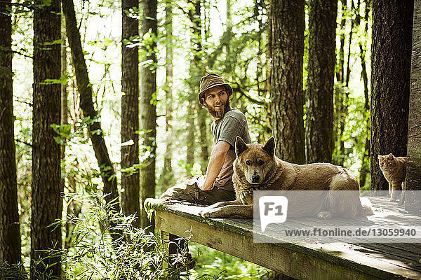 Mann schaut weg  während er mit Hund auf der Veranda gegen Bäume sitzt