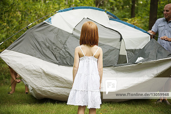 Rückansicht eines Mädchens  das den Vater beim Zeltmachen im Wald beobachtet