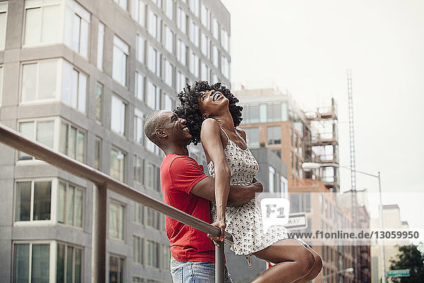 Fröhliches Paar am Geländer gegen Gebäude in der Stadt