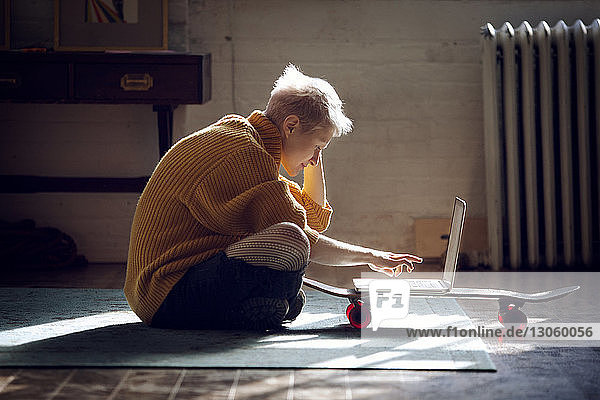 Junge Frau benutzt Laptop-Computer  während sie zu Hause auf dem Boden sitzt