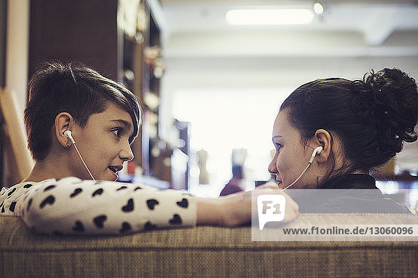 Freunde hören Musik über Kopfhörer  während sie im Café auf dem Sofa sitzen