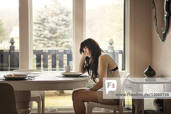 Seitenansicht einer Frau  die zu Hause auf einem Stuhl am Tisch sitzt